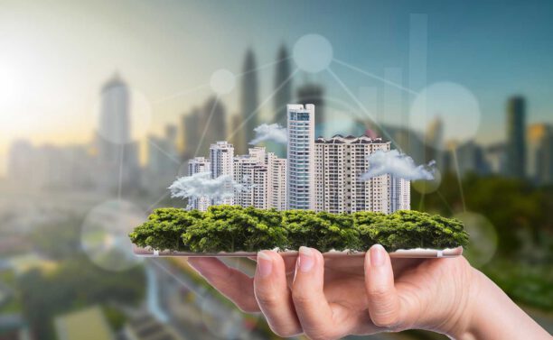 Hand hält Gebäudekomplex, welcher symbolisch für Smart Buildings steht.