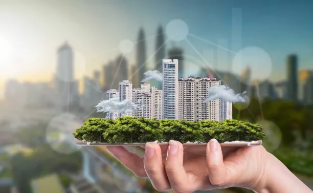 Hand hält Gebäudekomplex, welcher symbolisch für Smart Buildings steht.